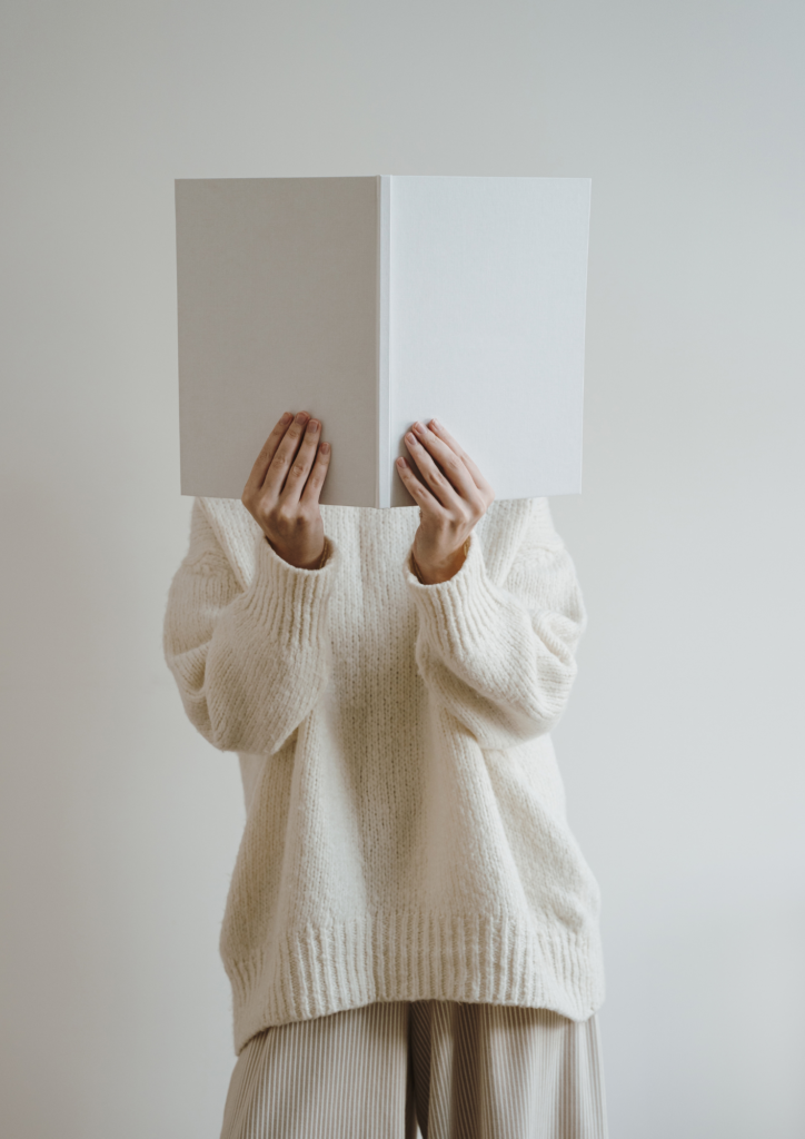 woman looking at open book with face covered by book cool beige aesthetic