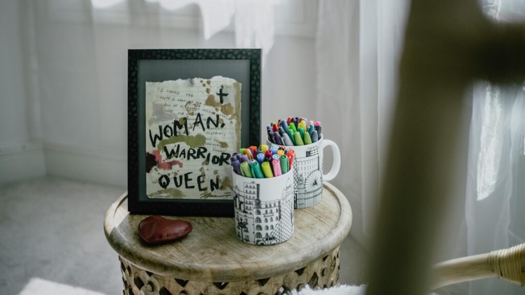 Powerful Affirmations for Success art motivational art peice reading 'Woman, Warrior, Queen' on a table with colorful pens in mugs.