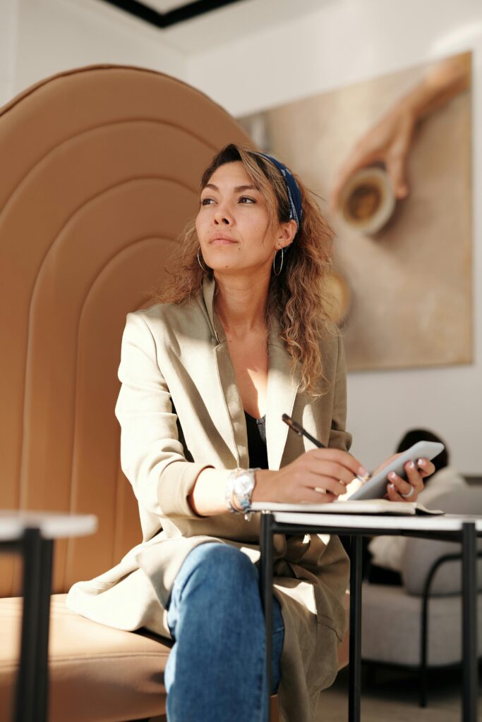 Intentional Planning; Confident woman in blazer taking notes with pen and smartphone in cafe.