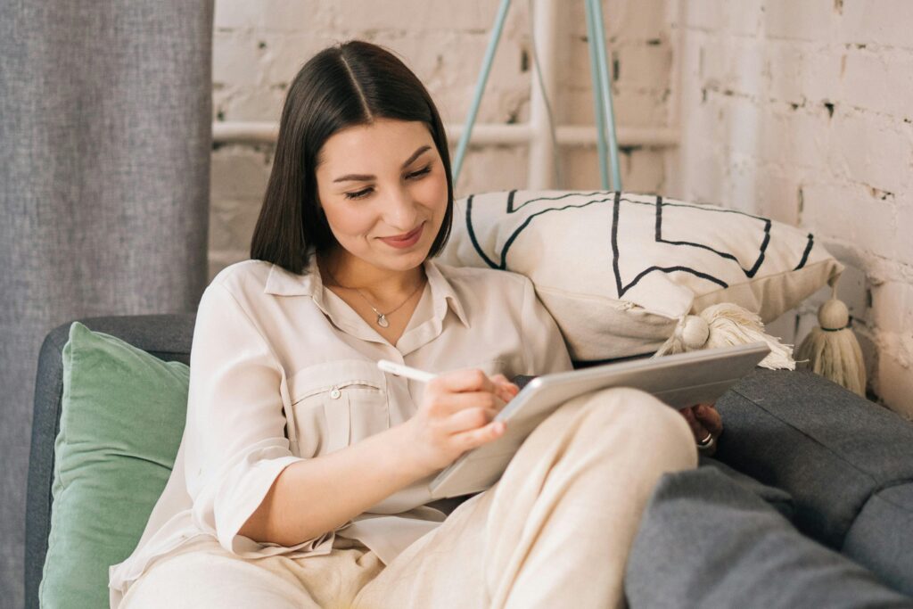 pexels-photo-4963062-4963062 Smiling woman using tablet on sofa in a cozy home setting, enjoying work from home.