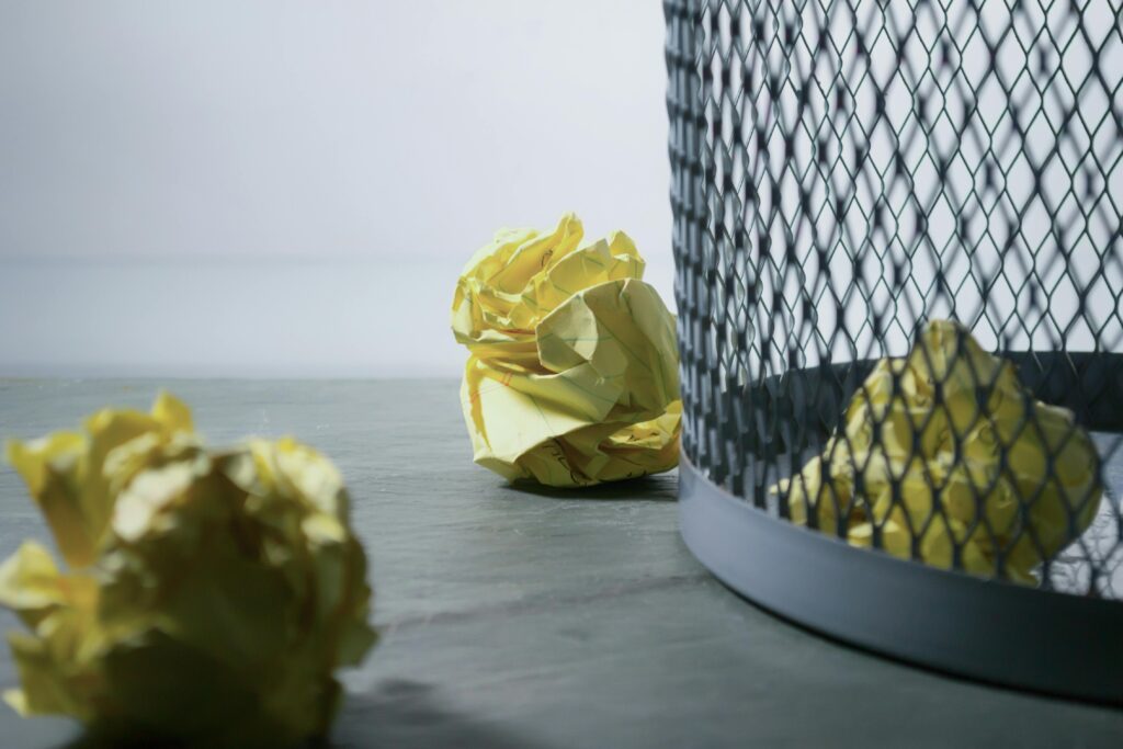 5 great reasons to use digital planners - Close-up of crumpled yellow paper around a mesh trash bin, symbolizing rejected ideas or recycling.